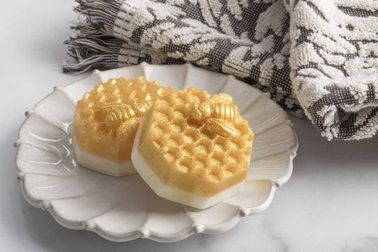 Two bars of soap with a honeycomb design, placed on a white plate, with a patterned cloth in the background.