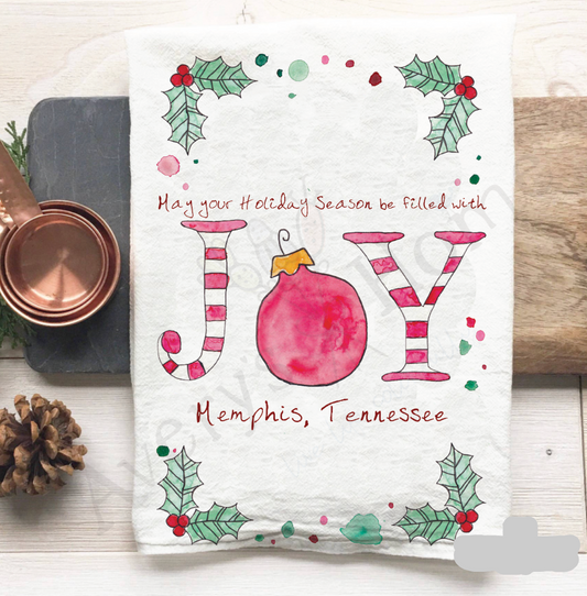 Holiday-themed kitchen towel with decorative text and Christmas elements on a wooden surface.